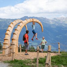 Three children are playing on a large wooden sculpture in the Alps.