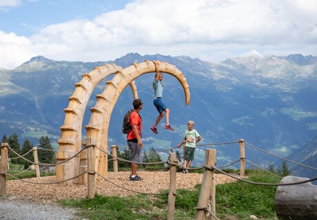 Three children are playing on a large wooden sculpture in the Alps.