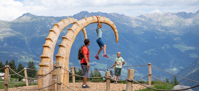 Three children are playing on a large wooden sculpture in the Alps.