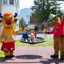 Four kids play with two mascots on a swing.