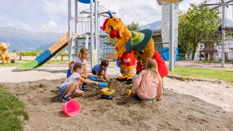 Children playing in a sandbox with mascots on a playground.