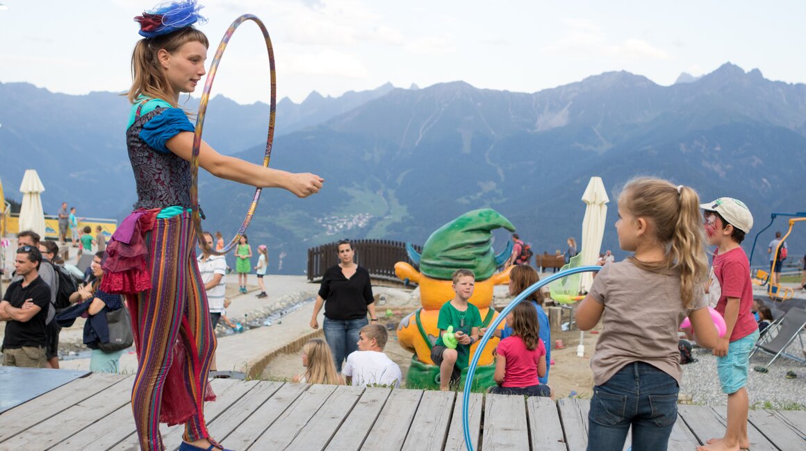 A performer with hoops on stage, children watching.