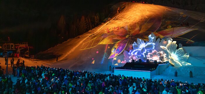 A large crowd enjoying an impressive light show on a snowy slope.