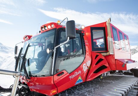 Close-up of a red snow groomer on snow-covered terrain.