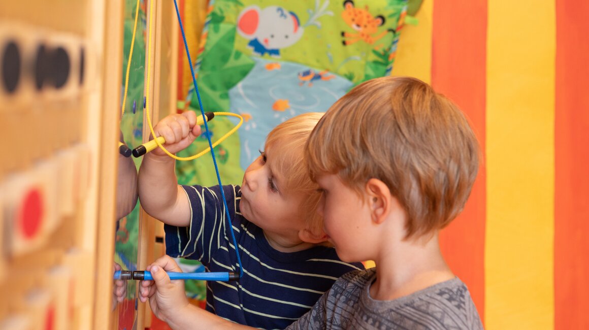 Twee kinderen interacteren met een kleurrijke wand vol speelmaterialen.