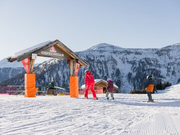 Children learning to ski at a snow school with mountains in the background.
