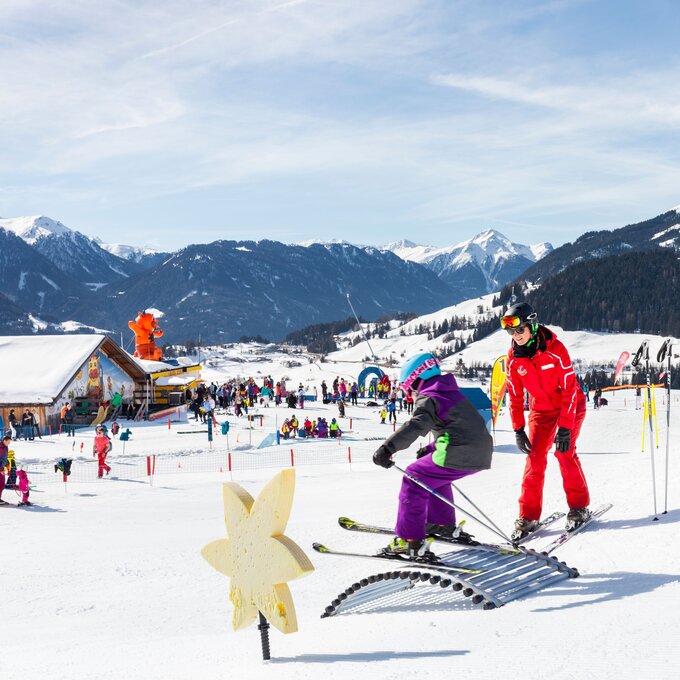 A child learns to ski with an instructor against a beautiful winter landscape.