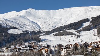 Winterliche Berglandschaft mit verschneiten Hügeln und Hütten.