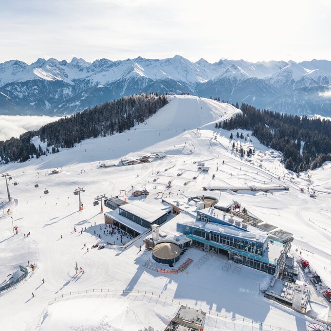 Luftaufnahme eines Skigebiets mit Pistenskifahrern und Bergen.
