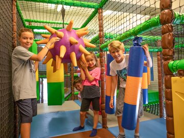 Vier Kinder spielen in einem bunten Indoor-Spielplatz mit großen, weichen Spielzeugen.