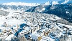 Luftaufnahme eines verschneiten Dorfes umgeben von Bergen.