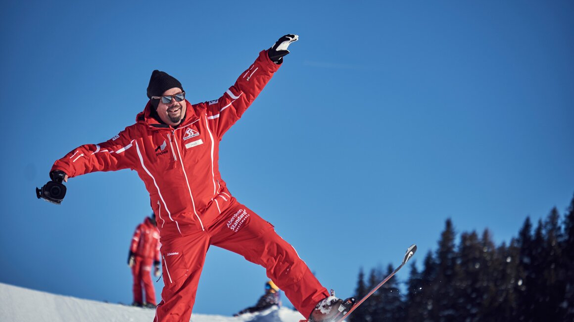 A man in red skiing gear having fun with a camera.