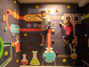 Two kids climbing on a colorful climbing wall indoors.