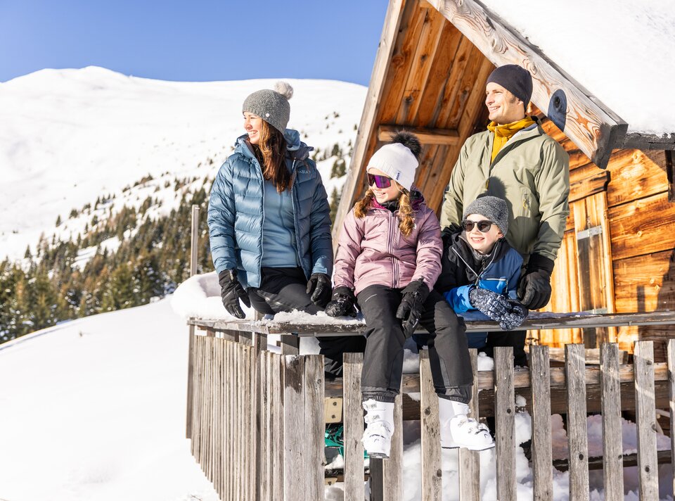 Family posing in front of a mountain cabin in the snow.