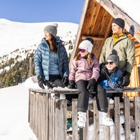 Familie posiert vor einer Berghütte im Schnee.