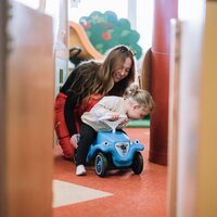 Eine Mutter hilft ihrem Kind mit einem Spielzeugauto zu fahren.