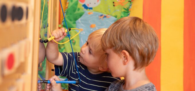 Twee kinderen interacteren met een kleurrijke wand vol speelmaterialen.