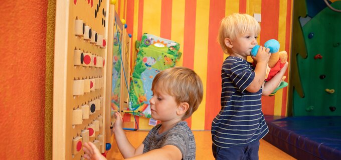 Twee kinderen spelen met een houten speelgoed in een kleurrijke kamer.