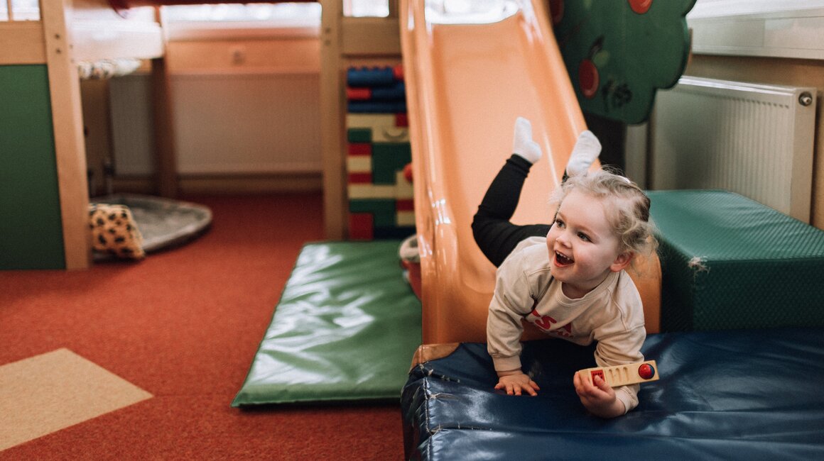 A young child happily plays on a slide in a playground area.