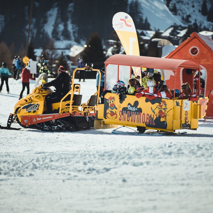 A snowmobile with passengers on a snowy slope.