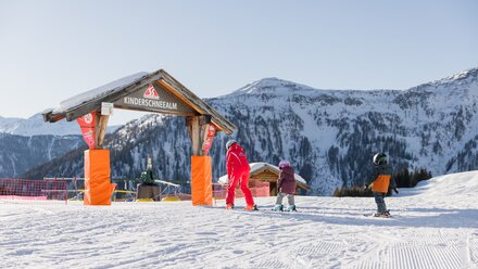 Children learning to ski at a snow school with mountains in the background.