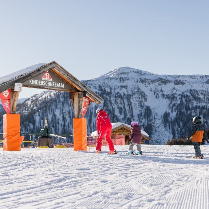 Children learning to ski at a snow school with mountains in the background.