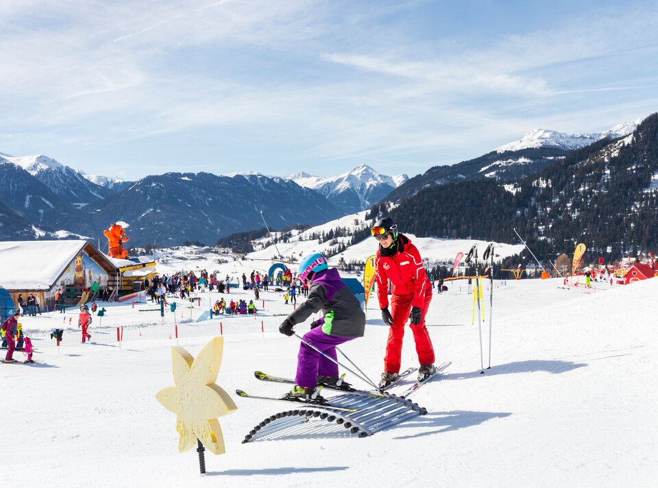 A child learns to ski with an instructor against a beautiful winter landscape.