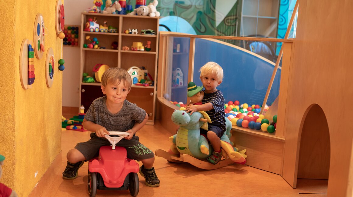 Two boys are playing in the playroom with toy vehicles.
