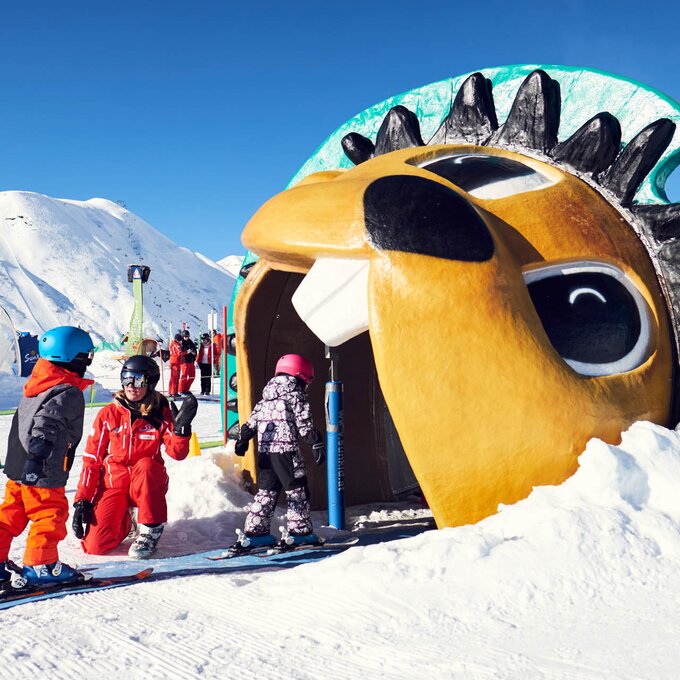 Three kids in ski gear in front of a big, colorful snow tunnel.