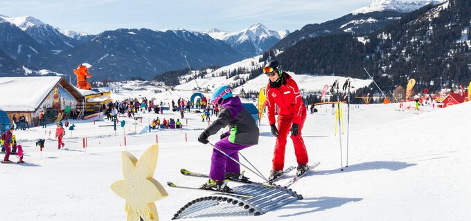 A child learns to ski with an instructor against a beautiful winter landscape.