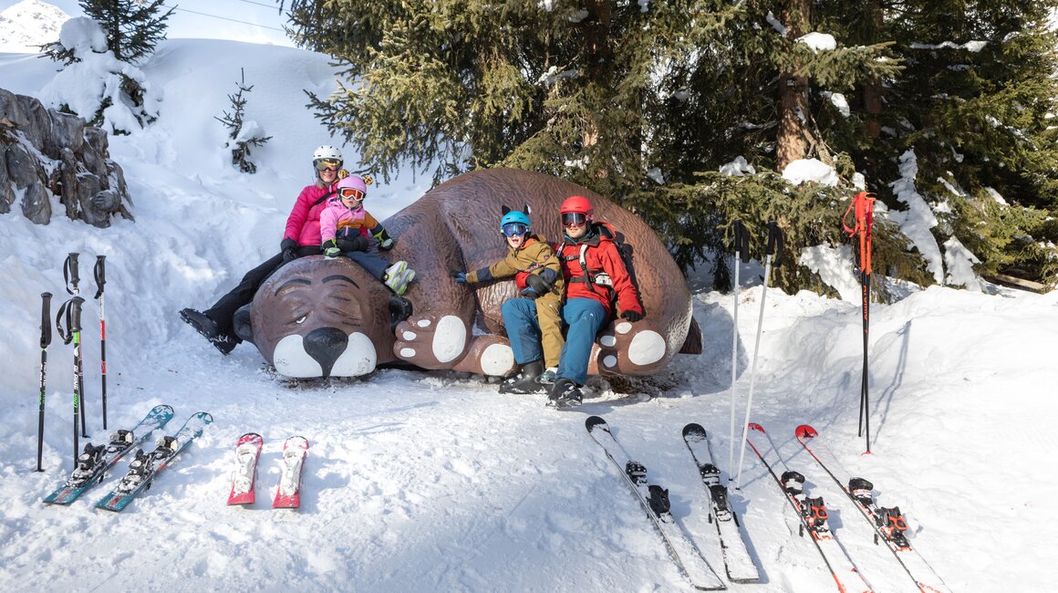 Familie sitzt auf einer Bären-Skulptur im Schnee.