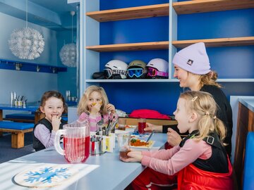 Familie genießt Snacks und Getränke in einer Berghütte.