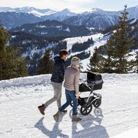 Paar spaziert mit Kinderwagen bei Schnee in den Bergen.