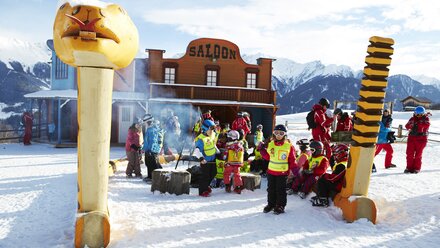 Group of children in ski attire gathered in front of a saloon in the snow.