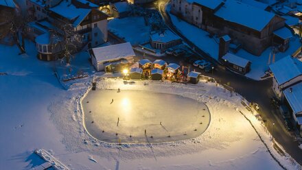 Skaters on a lit rink in a snowy setting.