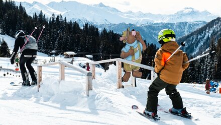 Child in ski gear in front of a bear figure in the Alps.