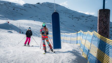 Two skiers, one in a colorful suit and one in black, skiing down a snowy slope.