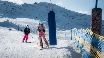 Two skiers, one in a colorful suit and one in black, skiing down a snowy slope.