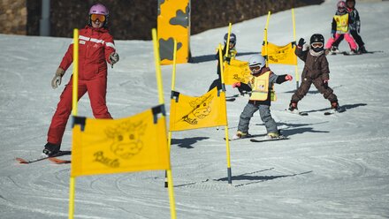 A ski instructor guides kids through a course marked by flags.