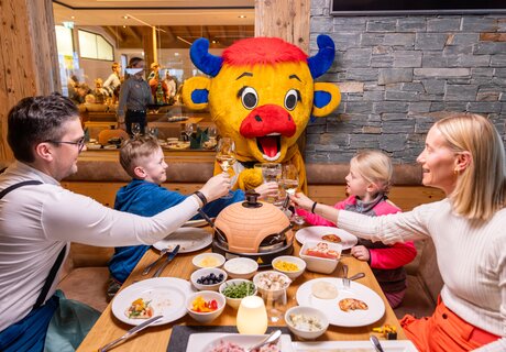 Family cheers with drinks while a mascot smiles.
