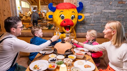 Family cheers with drinks while a mascot smiles.