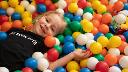 A smiling child is lying in a colorful ball pit full of balls.