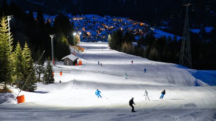 Night view of a ski slope with skiers and a lit village.