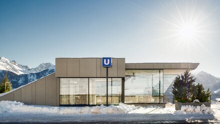 A modern glass subway station in the snow with mountain views.