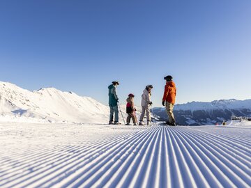 Eine Familie mit Skiausrüstung genießt einen sonnigen Tag auf der Piste.