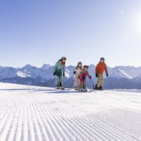 Familie mit zwei Kindern beim Skifahren auf verschneiter Piste.