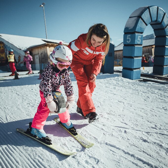 Ein Kind lernt mit einer Lehrerin das Skifahren auf einem verschneiten Hang.