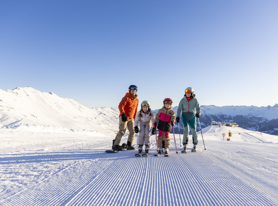 Eine Familie posiert auf einer Piste im Schnee beim Skifahren.