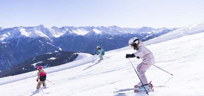 Three skiers on a snowy slope with mountains in the background.
