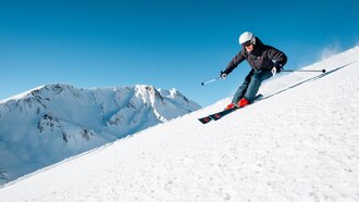 Skier on snowy slope with mountains in the background.